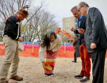 Denise Bright Dove Ashton-Dunkley (center) pours water on the ground where Calder Gardens will be constructed during a ritual drawn from Nanticoke Lenni-Lenape tradition. Joining her are Urie Ridgeway (left), philanthropist Joseph Neubauer (right) whose efforts brought the Calder museum to fruition, and Alexander S. C. Rower, grandson of the sculptor Alexander Calder. (Emma Lee/WHYY)