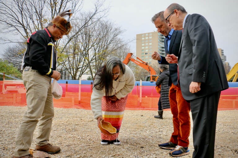 Denise Bright Dove Ashton-Dunkley (center) pours water on the ground where Calder Gardens will be constructed during a ritual drawn from Nanticoke Lenni-Lenape tradition. Joining her are Urie Ridgeway (left), philanthropist Joseph Neubauer (right) whose efforts brought the Calder museum to fruition, and Alexander S. C. Rower, grandson of the sculptor Alexander Calder. (Emma Lee/WHYY)