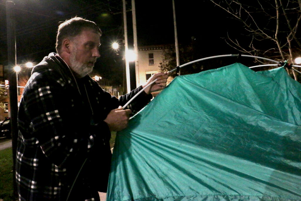 A man pitches a tent at night.