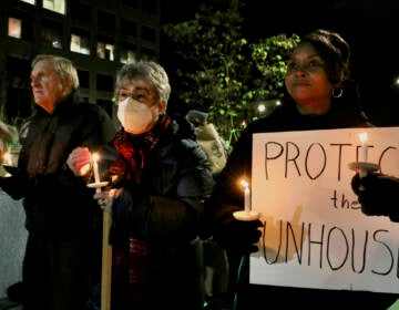 A group of people hold candles, with one person holding a sign that reads, 