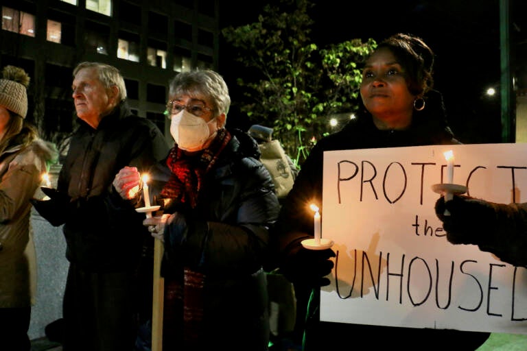 A group of people hold candles, with one person holding a sign that reads, 