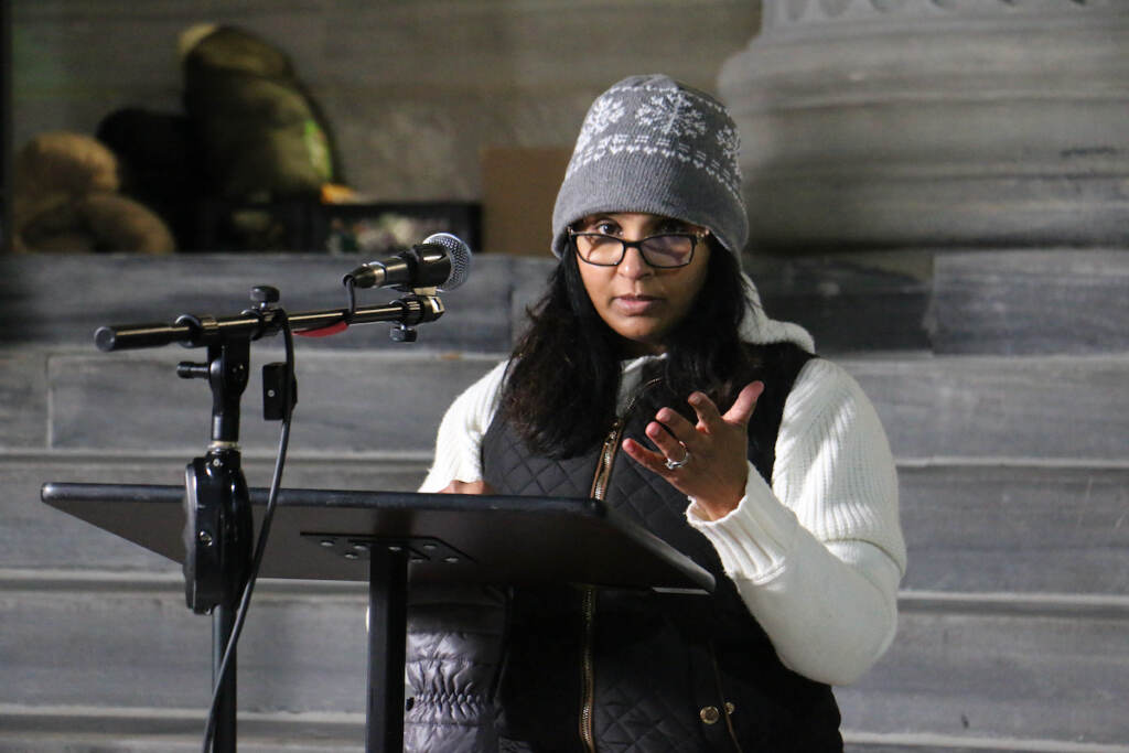 A woman stands at a podium wearing a winter hat and jacket.