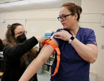 A person applies a tourniquet to a nurse instructor's arm.