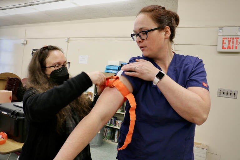 A person applies a tourniquet to a nurse instructor's arm.