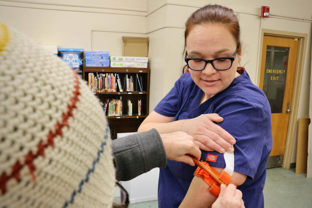 A person applies a tourniquet to a nurse instructor's arm.