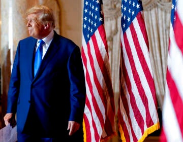 Donald Trump stands next to several U.S. flags.