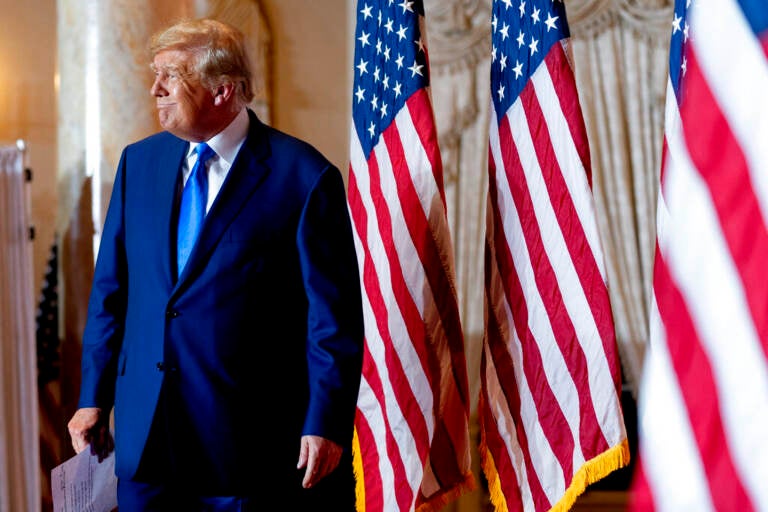 Donald Trump stands next to several U.S. flags.