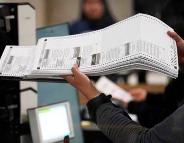 A person holds ballots in their hand as they feed them into a machine.