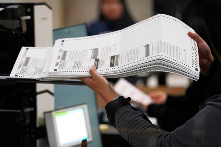 A person holds ballots in their hand as they feed them into a machine.