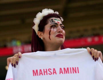 An Iran team supporter cries as she holds a shirt that reads ''Mahsa Amini'' prior to the start of the World Cup group B soccer match between Wales and Iran, at the Ahmad Bin Ali Stadium in Al Rayyan, Qatar, Friday, Nov. 25, 2022. (AP Photo/Alessandra Tarantino)