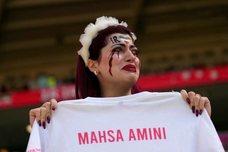 An Iran team supporter cries as she holds a shirt that reads ''Mahsa Amini'' prior to the start of the World Cup group B soccer match between Wales and Iran, at the Ahmad Bin Ali Stadium in Al Rayyan, Qatar, Friday, Nov. 25, 2022. (AP Photo/Alessandra Tarantino)