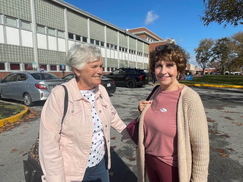 Two women pose together outside of a building.