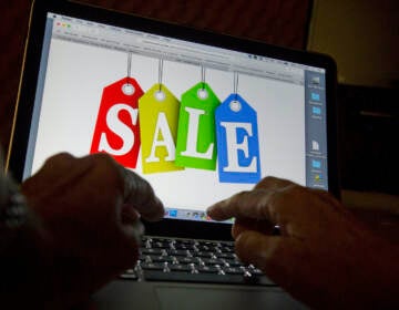 A person's hands are seen on a keyboard in front of a computer screen that has the word 'SALE' written on it