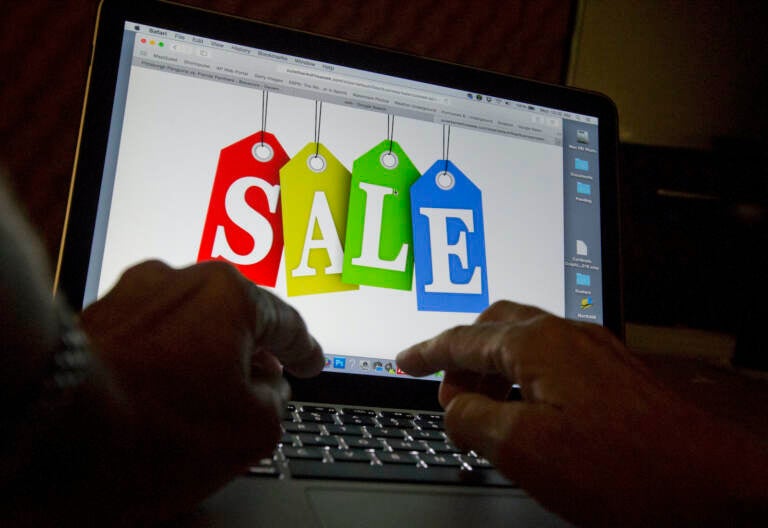 A person's hands are seen on a keyboard in front of a computer screen that has the word 'SALE' written on it