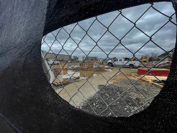 Construction is seen through a ripped tarp on a chainlink fence