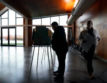 A voter walks to cast their ballot as another fills his out at the Eleanor Boathouse polling place on the Southside of Chicago, Tuesday, Nov. 8, 2022. (AP Photo/Charles Rex Arbogast)