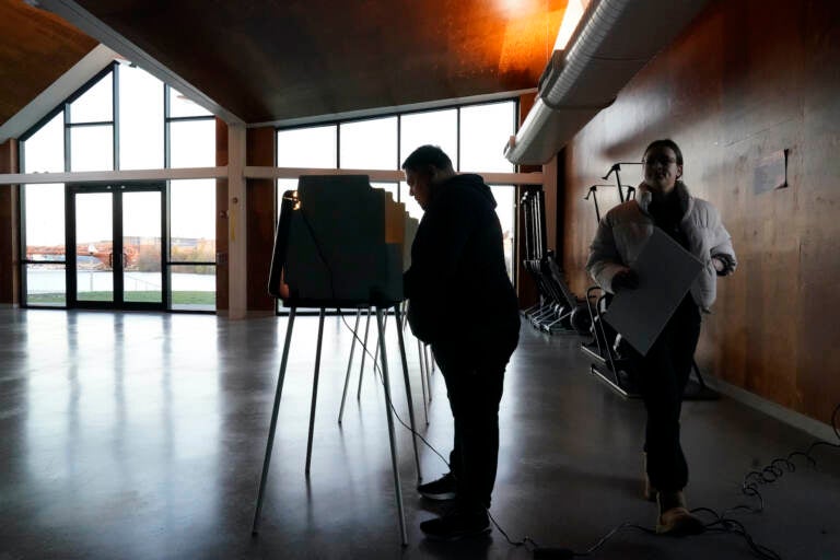 A voter walks to cast their ballot as another fills his out at the Eleanor Boathouse polling place on the Southside of Chicago, Tuesday, Nov. 8, 2022. (AP Photo/Charles Rex Arbogast)