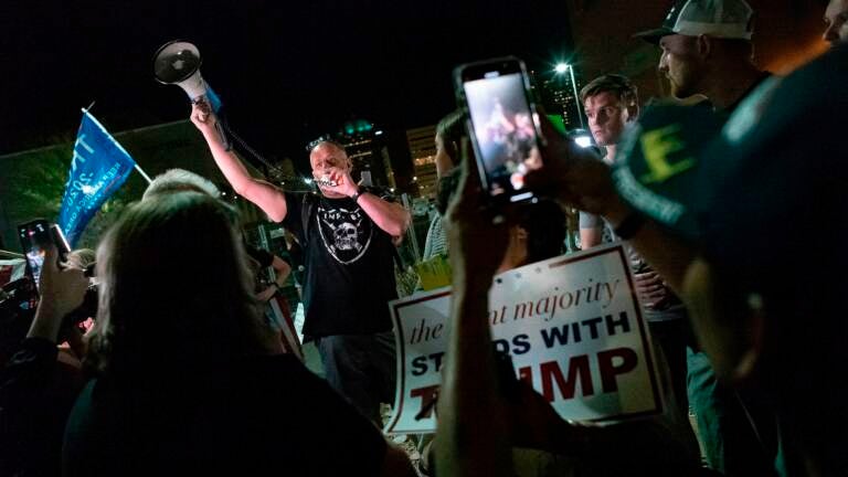 A man yells into a bullhorn surrounded by other people.