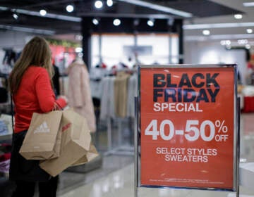 A person with shopping bags walks by a sign advertising Black Friday sales.