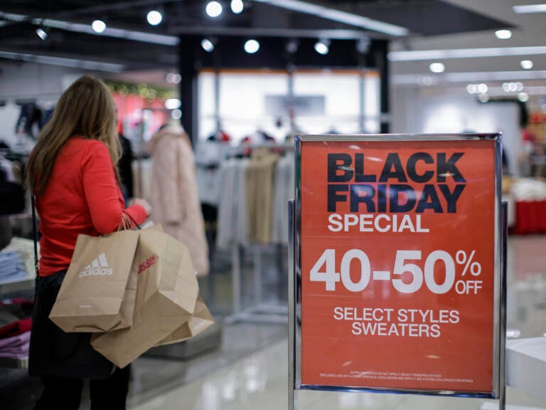 A person with shopping bags walks by a sign advertising Black Friday sales.