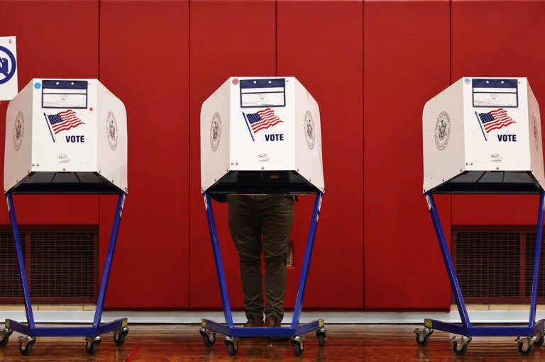 A person's legs are visible as they stand behind a voting booth.