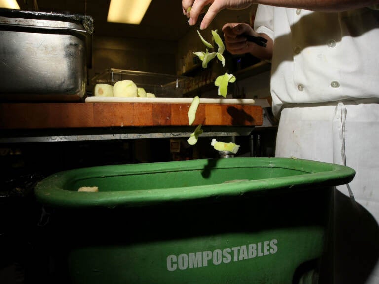 A person drops apple peels into a green bin that reads 