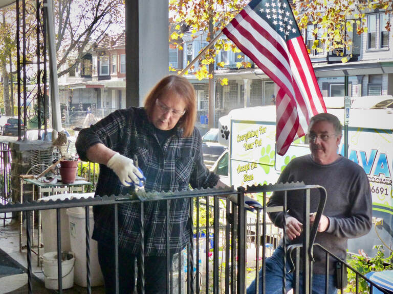 People paint the railing on a porch, with the U.S. flag flying in the background.