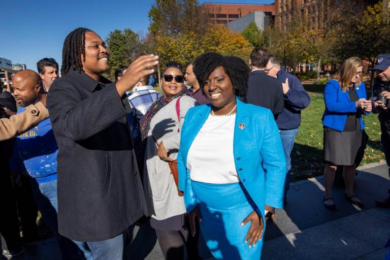 Rep. McClinton, wearing a bright blue suit, smiles in the midst of other legislators on a sunny day.