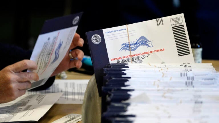 A person handles a mail ballot as a stack of mail ballots sit in front of them.