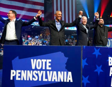 Shapiro, Obama, Biden, and Fetterman hold hands in front of a cheering crowd.