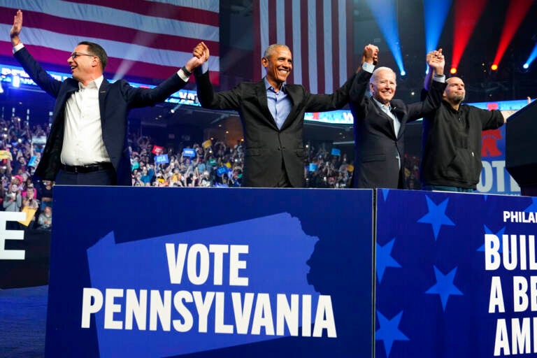 Shapiro, Obama, Biden, and Fetterman hold hands in front of a cheering crowd.