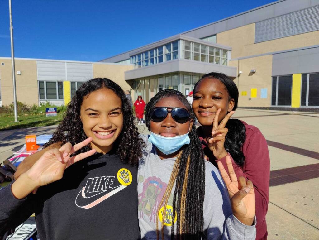 Three people smile and give the peace sign.