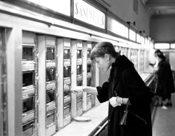 A black-and-white photo of Audrey Hepburn looking at an automat.