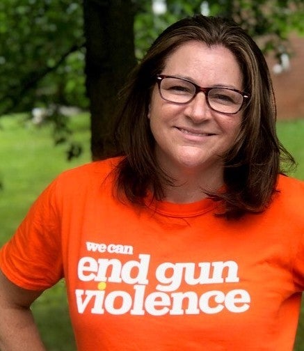 A woman poses for the camera wearing an orange T-shirt that reads "end gun violence."