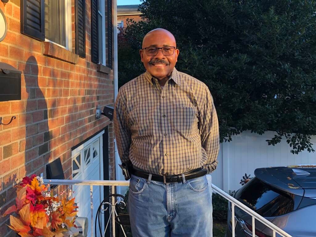 A man smiles next to his house.