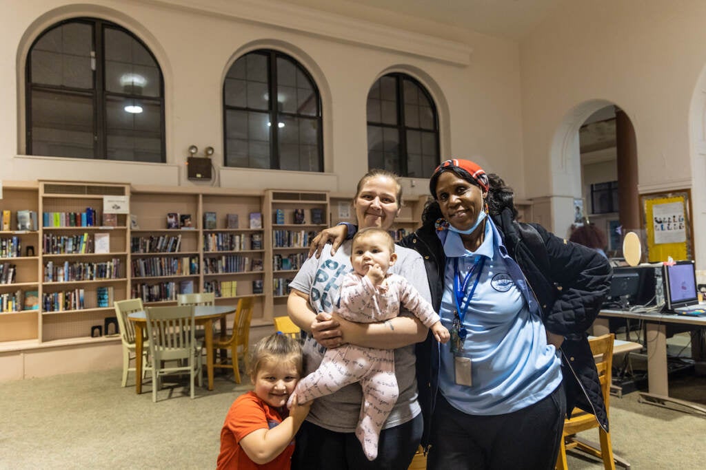 Two women pose with two children. A library is visible behind them.