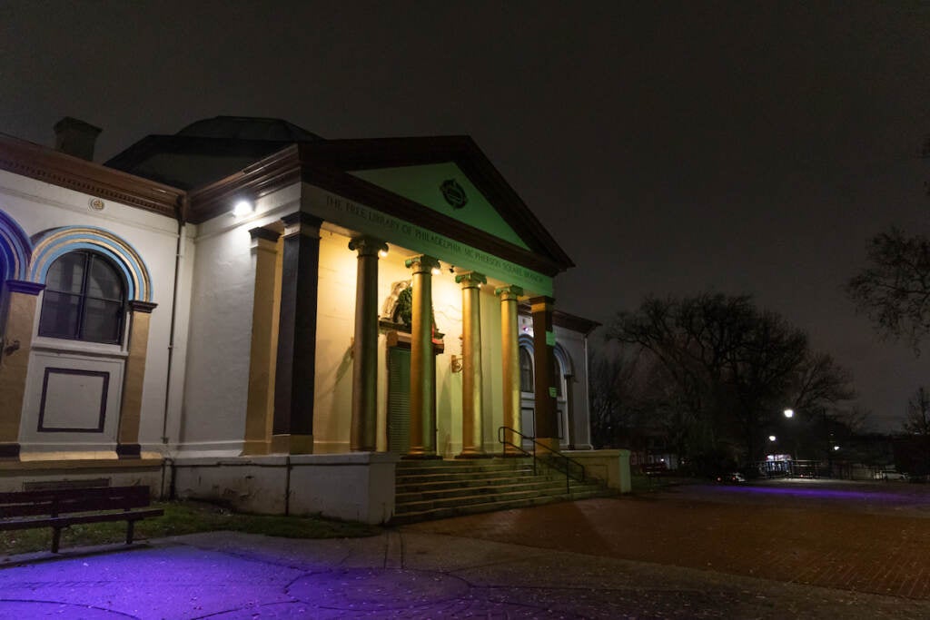 A library building is lit up at night in a park.