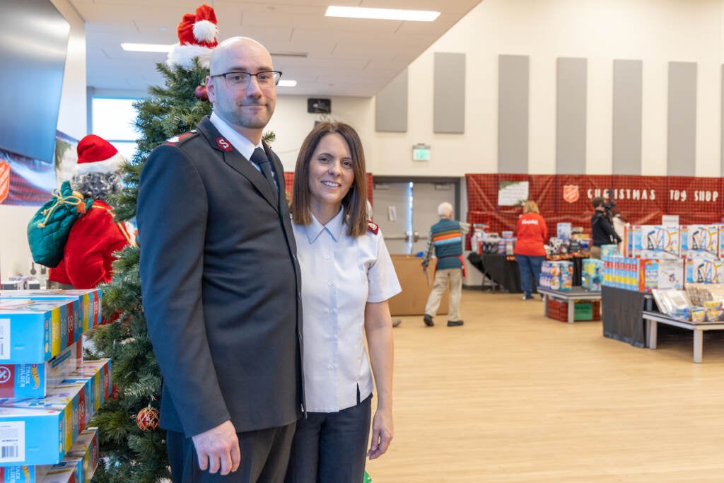 A man and woman stand in front of a Christmas tree in a large room.