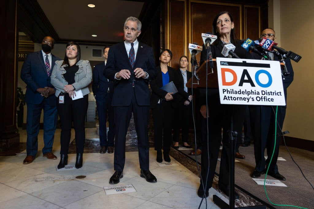 A woman speaks at a podium surrounded by other people.