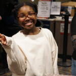 A girl gives the peace sign as she smiles.