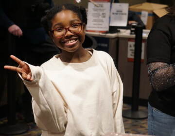 A girl gives the peace sign as she smiles.