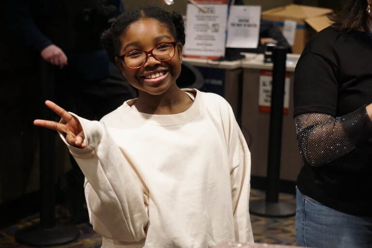 A girl gives the peace sign as she smiles.