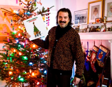 A person holds up an album, with a Christmas tree visible in the background.