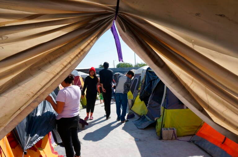 People walk around, as seen through the parted curtains of a tent.