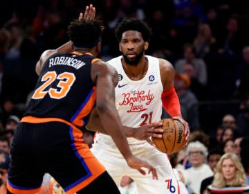 Philadelphia 76ers center Joel Embiid (21) looks to pass around New York Knicks center Mitchell Robinson during the first half of an NBA basketball game, Sunday, Dec. 25, 2022, in New York. (AP Photo/Adam Hunger)