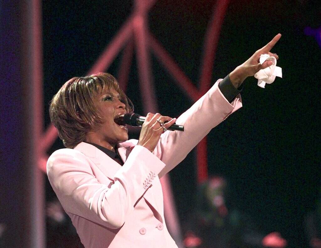 Singer Whitney Houston sings into a microphone while pointing into the air.