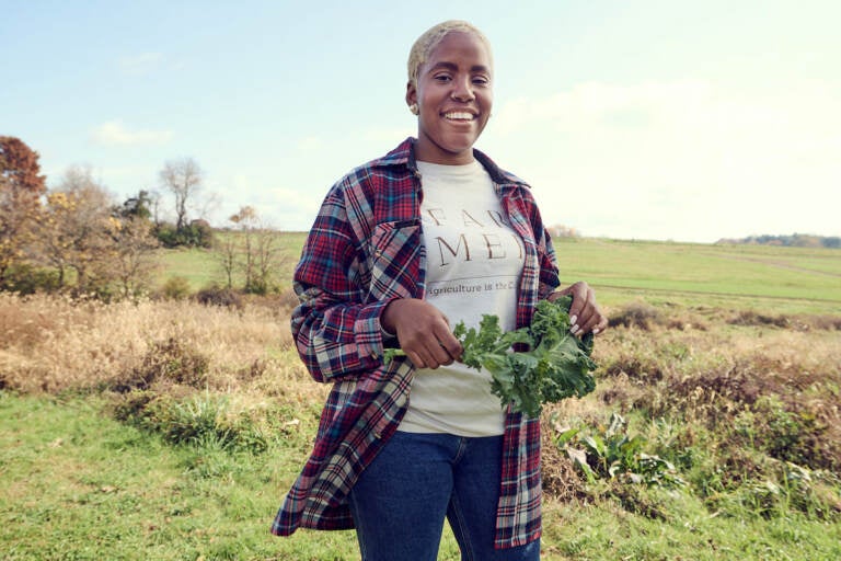 Christa Barfield stands with greens in her hand, with rolling fields in the background.