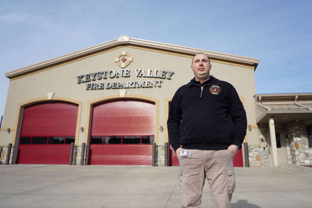 A man stands outside of a building that reads Keystone Valley Fire Department.