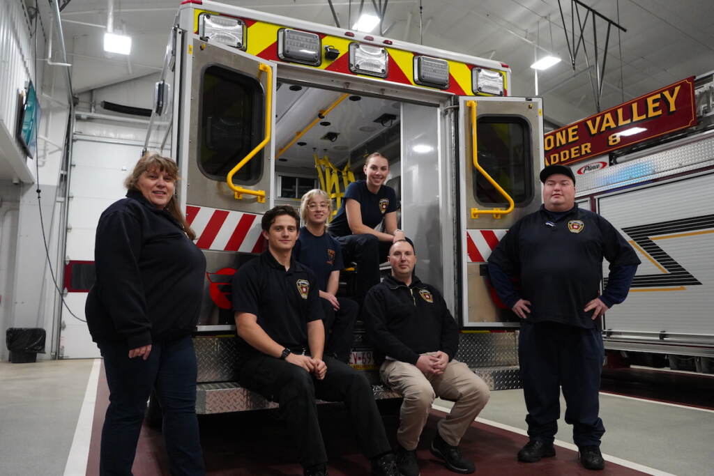 Several EMTs pose for a photo at the back of an ambulance.