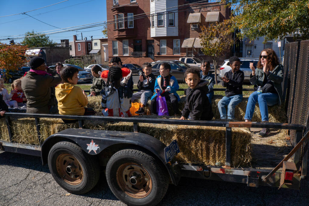 Children sit on a tractor trailer bed for a hay ride in a park.